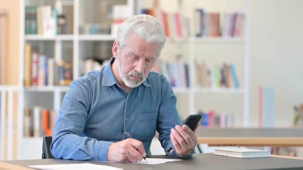 Old Businessman Using Smartphone and Doing Paperwork