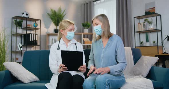 Doctor in Mask Hearing About Symptoms of Illness from Her Patient During her Home Visit