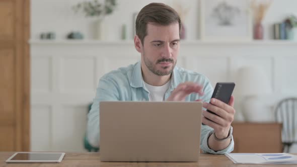 Young Man Using Smartphone and Laptop at Workplace