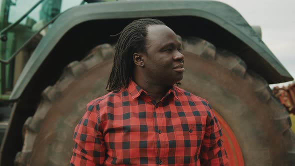 African Man, Farmer Standing in Front of the Tractor Wheel and Looking Around