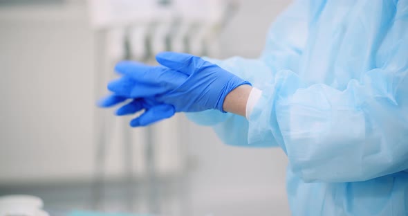 Doctor Puts Blue Protective Gloves on Hands at Healt Care Clinic