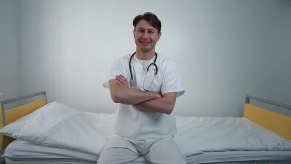 Portrait of Confident Doctor Crossing Hands Looking at Camera Smiling Sitting on Bed in Comfortable