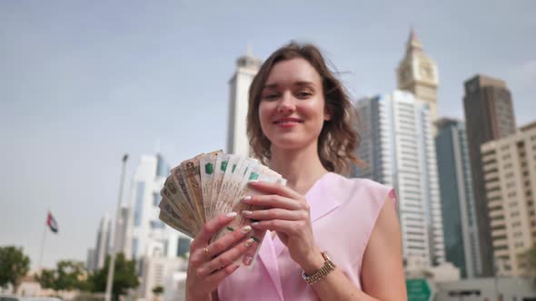 The Girl Holds in Her Hands the Money of the United Arab Emirates on the Background of the City