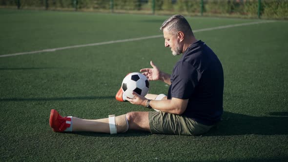 Side View Wide Shot Mature Sportsman Amputee Playing with Soccer Ball in Slow Motion Talking Sitting