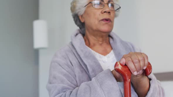 African american senior woman leaning on her walking stick while sitting on the bed at home