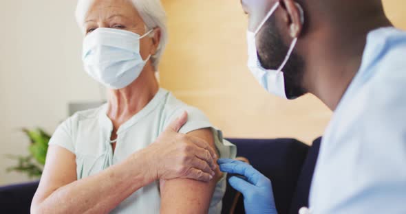 Video of african american male doctor in face mask vaccinating caucasian senior woman