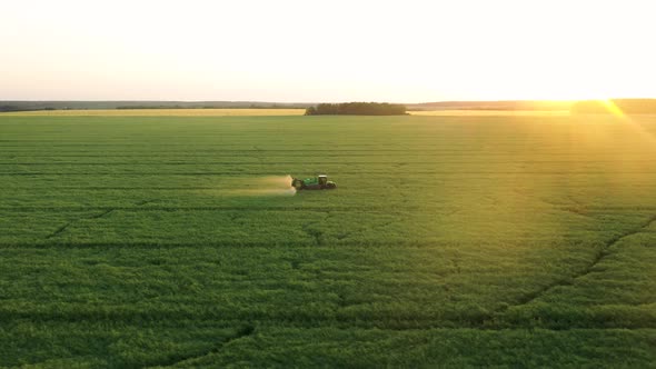 Farmer Tractor Sprays Fertilizers Over Field Of Agricultural Crops At Sunset