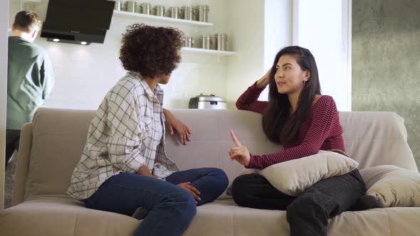 Two Girlfriends an AfricanAmerican and an Asian Chatting with Each Other While Sitting at Home on