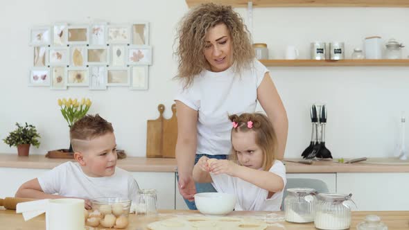 The Girl Breaks an Egg Into a Bowl on Her Own While She Cooks with Her Mother and Brother in the