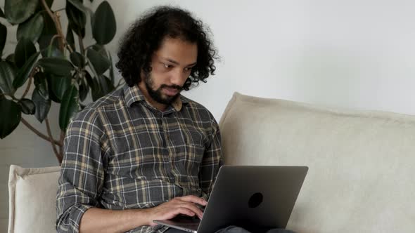 Close up of handsome man using laptop on sofa in living room. Working from home. Social distancing