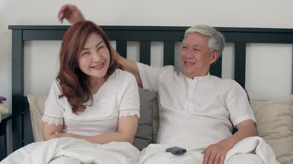 Asian elderly couple watching television enjoy love moment while lying on the bed.