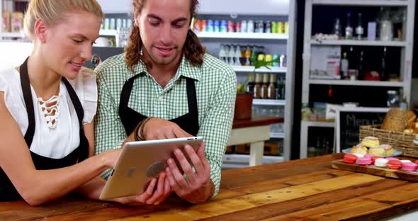 Smiling waiter and waitress standing at counter using digital