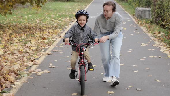 Happy Mother teaches child son to ride a bike on the bike path