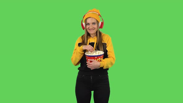 Modern Girl in Big Red Headphones Is Watching an Exciting Movie and Eating Popcorn. Green Screen