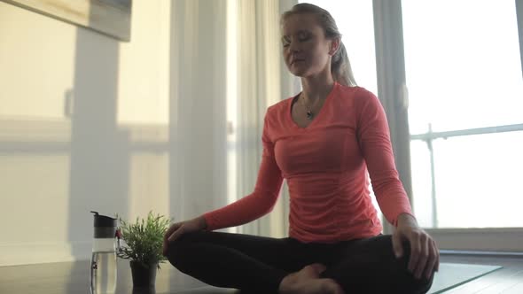 Woman in pink shirt and blank pants meditating and smiling