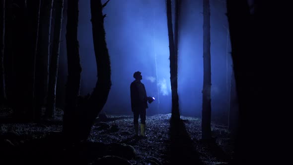 Man with lantern in night foggy forest.