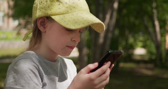 Little Girl Playing the Game on Her Smartphone While Sitting Outdoors