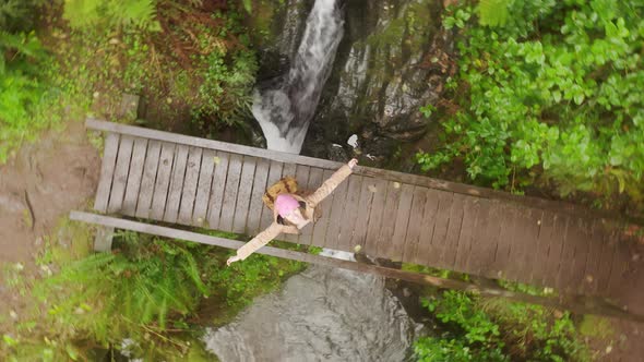 Happy Woman Tourist Spinning with Wide Opened Hands on Wooden Bridge Under Rain