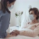 Home Caregiver With Face Mask Holding Hands of Female Senior Patient Lying in Bed at Nursing Home - VideoHive Item for Sale