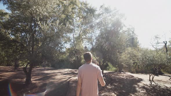 Forwards Tracking of Man Walking Through Park Towards Wooden Bridge