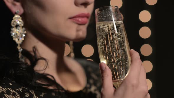 Woman Drinking Champagne From a Glass on a Background of Celebratory Lights at Night