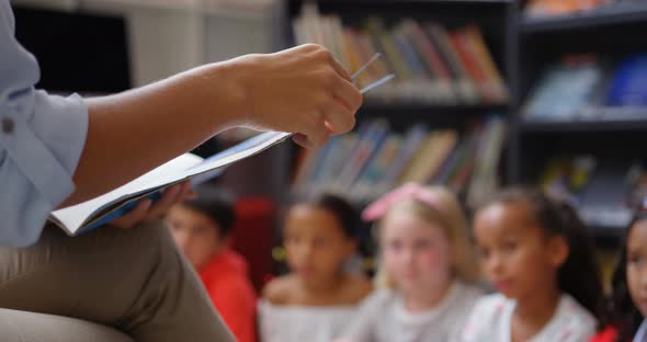 Mid section of female teacher teaching schoolkids in the school library 4k