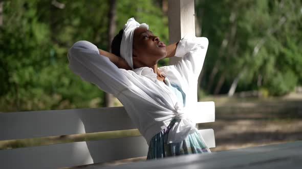 Thoughtful Confident African American Woman Sitting on Bench in Summer Park Looking Away