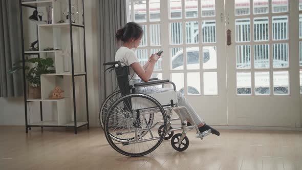 Asian Girl Sitting In A Wheelchair Using Mobile Phone At Home