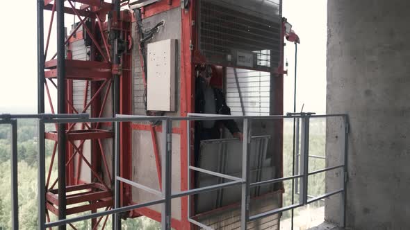 A Man Builder Opens the Doors of a Freight Construction Elevator