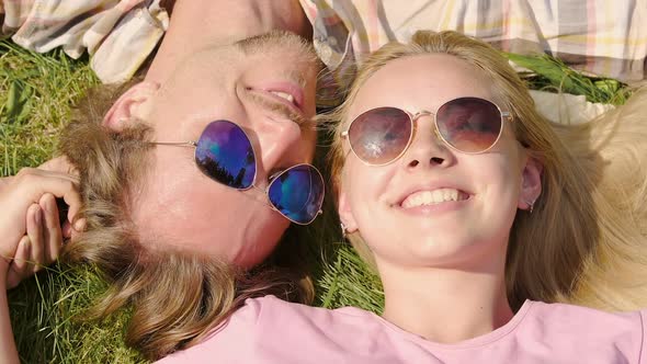 Man Tenderly Kissing Woman on Cheek, Lying on Grass Together, Watching Blue Sky