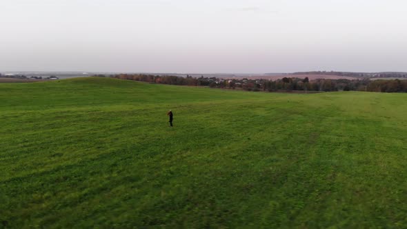 Top View of a Jumping Young Girl with Long Hair on a Large Green Meadow