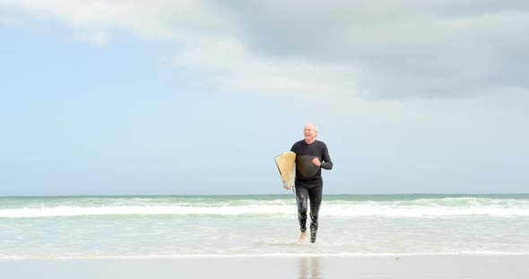 Front view of old caucasian senior man running with surfboard at beach 4k