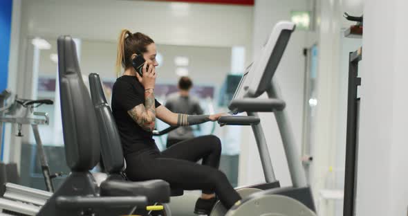 Woman Exercising with Elliptical Cross Trainer While Talking on Cellphone at gym.Side View, Slow