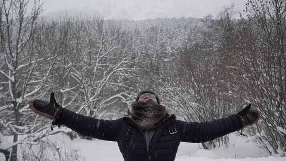 Content woman in outerwear outstretching arms in winter forest