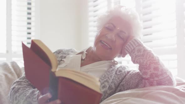 African american senior woman smiling while reading a book sitting on a bean bag at home