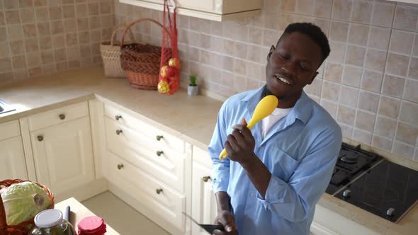 High Angle View Portrait of Joyful Young Man Singing in Cooking Utensil Looking at Camera Dancing in