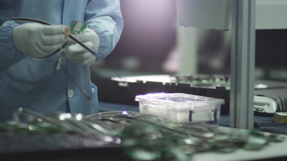 worker connects a cable to a TV electronic board on a factory assembly line