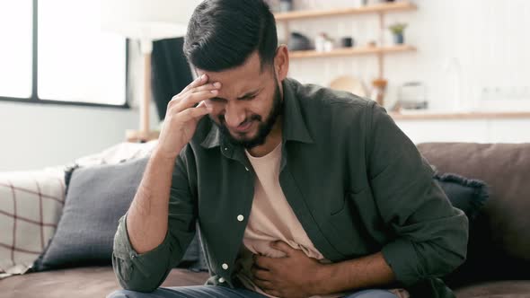 Sad Exhausted Guy of Indian and Arabian Ethnicity Sits on a Sofa in the Living Room Holds His Hands