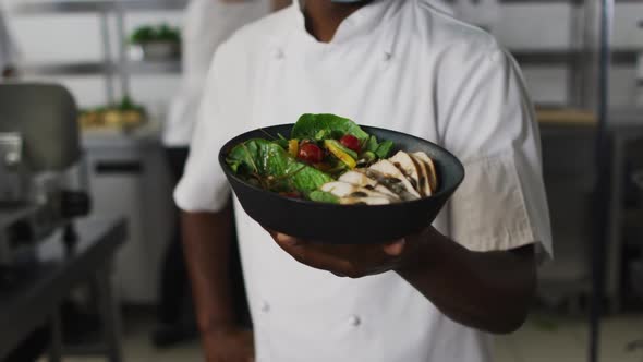 Portrait of african american male chef wearing face mask presenting dish