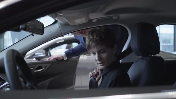 Beautiful Young Girl with a Short Haircut Examines New Auto While Sitting in Passenger Compartment