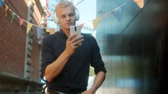 Carefree Guy Dancing Outdoors in City Street Wearing Headphones and Using Smartphone