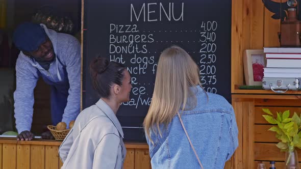 Two girls choosing snack by food booth menu