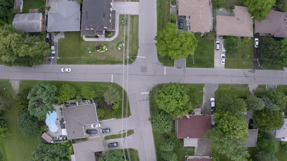 Top down view of white car driving through suburban neighborhood. Aerial drone view.