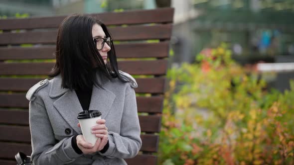 Adult Woman is Resting in Park in Daytime Holding Carton Cup with Hot Coffee From Street Cafe