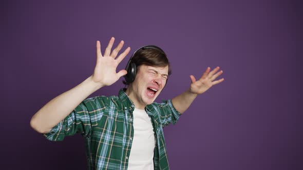 Emotional Man in Shirt Listening to Music on Headphones on Purple Background