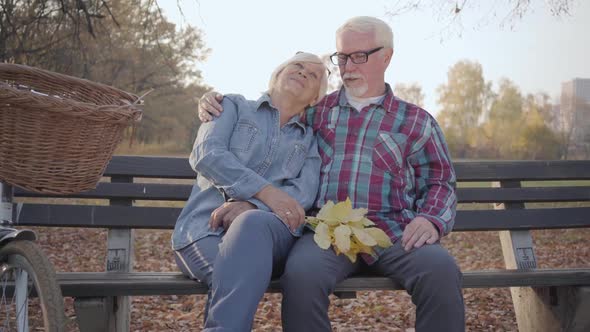 Portrait of a Happy Caucasian Retired Couple Sitting on the Bench in Sunlight and Talking