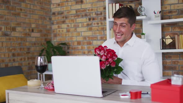 Caucasian man making video call using laptop holding bunch of flowers and smiling