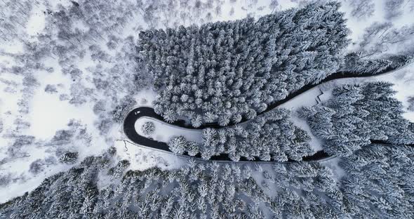 Overhead Aerial Top View Over Car Travelling on Hairpin Bend Turn Road in Mountain Winter Snow