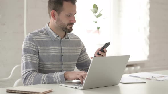 Adult Young Man Using Smartphone and Laptop