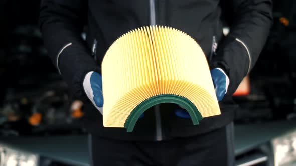 Car mechanic is holding a new yellow car air filter for maintenance at a service station